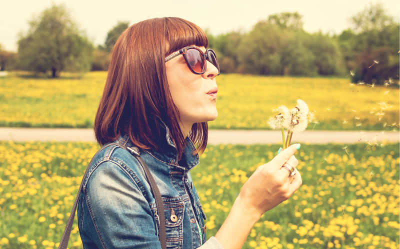 Chica con gafas de sol sujeta una flor con una mano mientras la sopla